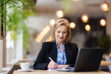 Zamówienia publiczne | Studia podyplomowe w Opolu | Uniwersytet WSB Merito Opole: Uczestniczka studiów podyplomowych robi notatki siedząc przy biurku