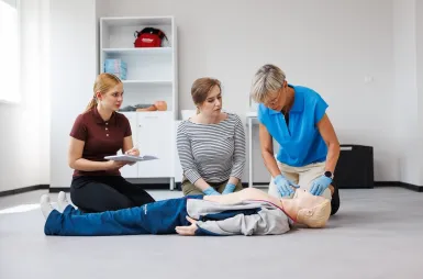 Laboratoria i pracownie | Uniwersytet WSB Merito Opole: Pracownia pierwszej pomocy: dwie studentki uczą się od pani profesor o tym, jak poprawnie przeprowadzać resuscytację na manekinie przedstawiającym dorosłego mężczyznę