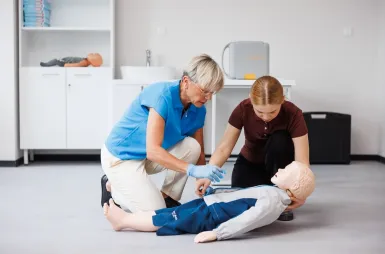 Laboratoria i pracownie | Uniwersytet WSB Merito Opole: Pracownia pierwszej pomocy: studentka uczy się od pani profesor o tym, jak poprawnie przeprowadzać resuscytację na manekinie przedstawiającym dziecko