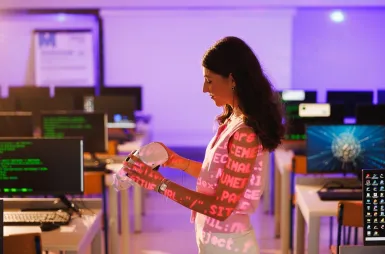 Laboratoria i pracownie | Uniwersytet WSB Merito Opole: Pracownia VR, studentka z okularami VR i kontrolerami stoi w sali komputerowej