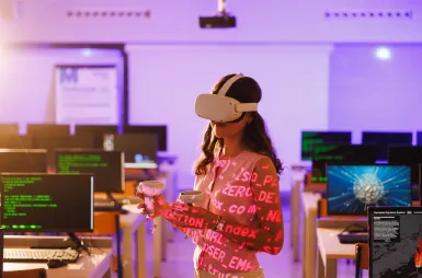 Laboratoria i pracownie | Uniwersytet WSB Merito Opole: Pracownia VR, studentka z okularami VR i kontrolerami stoi w sali komputerowej