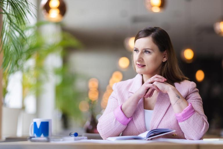 Zniżki i dofinansowania | Uniwersytet WSB Merito Opole: Uczestniczka studiów podyplomowych Uniwersytetu WSB Merito Opole. Siedzi przy biurku, patrzy w dal.