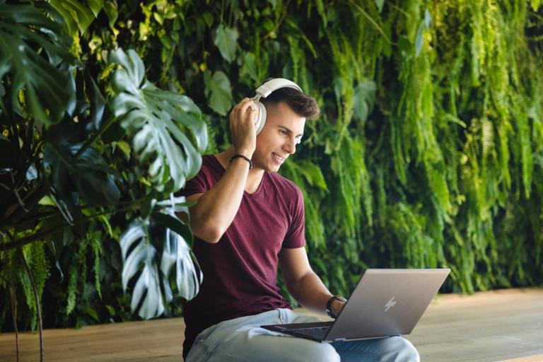 Media i komunikacja w biznesie | Studia I stopnia w Opolu | Uniwersytet WSB Merito Opole: chłopak siedzi z laptopem w słuchawkach wśród zieleni