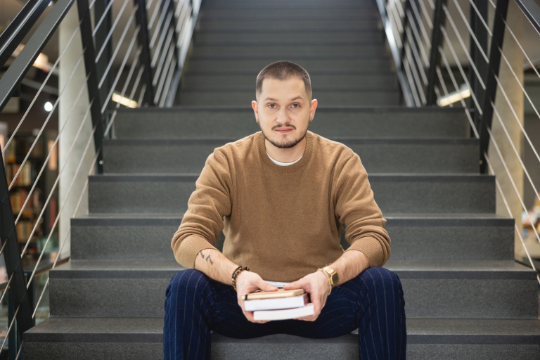 Management | Studia I stopnia w Opolu | Uniwersytet WSB Merito Opole: Student siedzący na schodach biblioteki, trzyma książki
