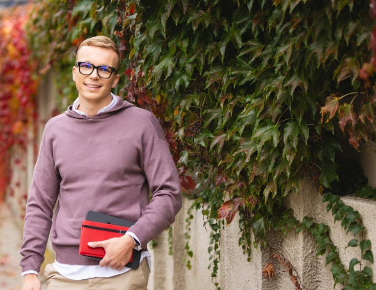 Wywiad i detektywistyka | Studia II stopnia ze studiami podyplomowymi  | Uniwersytet WSB Merito Opole: Student stojący na zewnątrz, trzyma książki