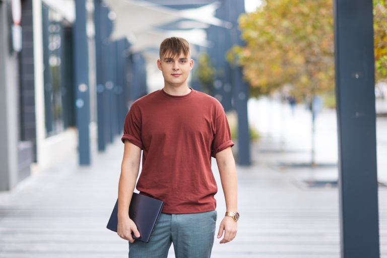 Stypendia i zniżki | Uniwersytet WSB Merito Opole: Student stojący na zewnątrz, trzyma laptopa