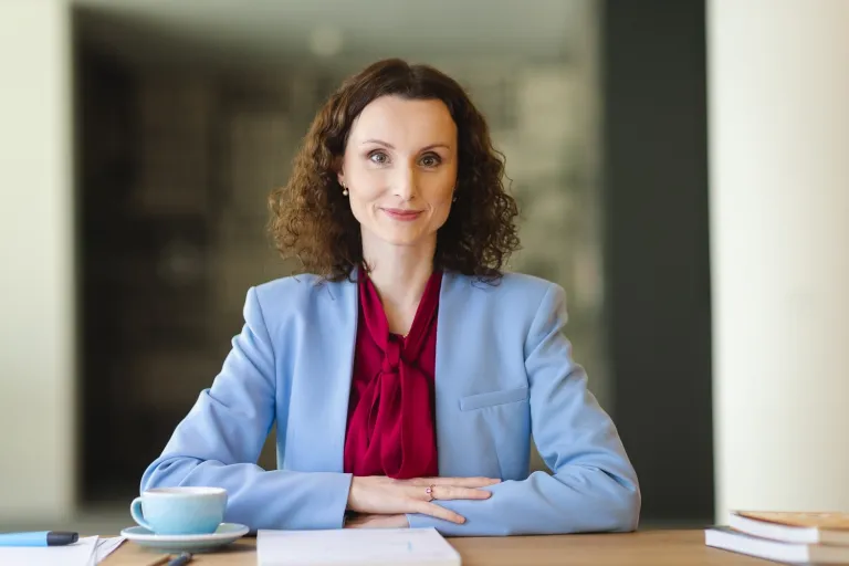 Audyt wewnętrzny i controlling | Studia podyplomowe w Opolu | Uniwersytet WSB Merito Opole: Kobieta siedząca za biurkiem, na biurku leżą książki, notesy i filiżanka kawy