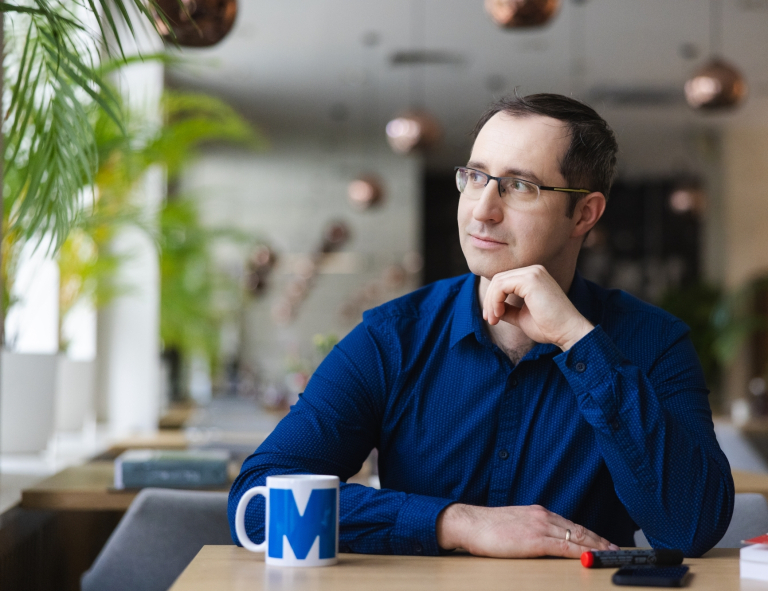 Bezpieczeństwo narodowe | Studia podyplomowe w Opolu | Uniwersytet WSB Merito Opole: Mężczyzna siedzący w kawiarni, na stole stoi kubek z logotypem Merito