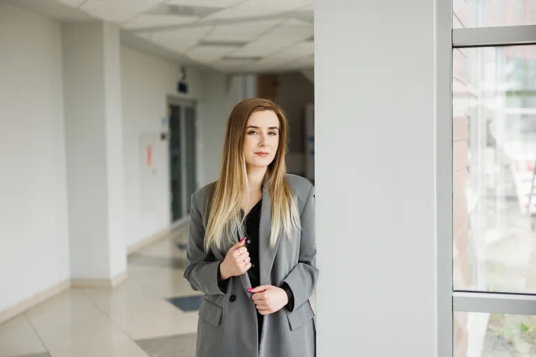 Wizaż i stylizacja z elementami charakteryzacji | Studia I stopnia w Opolu | Uniwersytet WSB Merito Opole: Dziewczyna w szarej marynarce stojąca na korytarzu uczelni