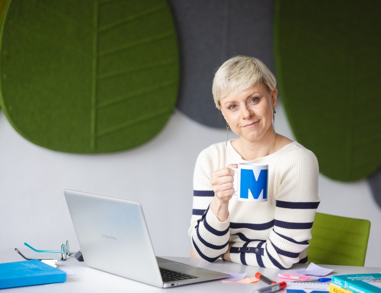 AI - uniwersalne kompetencje jutra | Studia podyplomowe w Opolu | Uniwersytet WSB Merito Opole: Kobieta siedząca przy biurku, w dłoni trzyma kubek