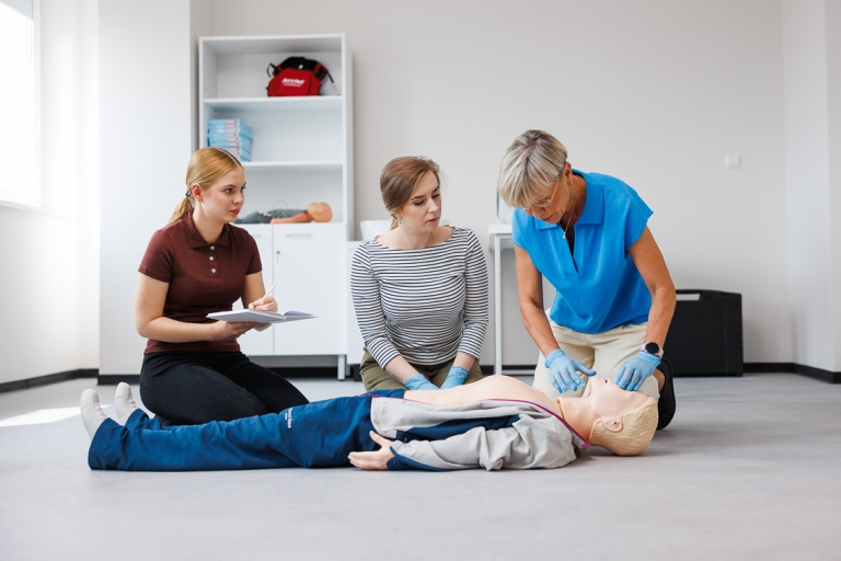 Administracja i bezpieczeństwo wewnętrzne | Studia II stopnia w Opolu | Uniwersytet WSB Merito Opole: Pracownia pierwszej pomocy: dwie studentki uczą się od pani profesor o tym, jak poprawnie przeprowadzać resuscytację na manekinie przedstawiającym dorosłego mężczyznę