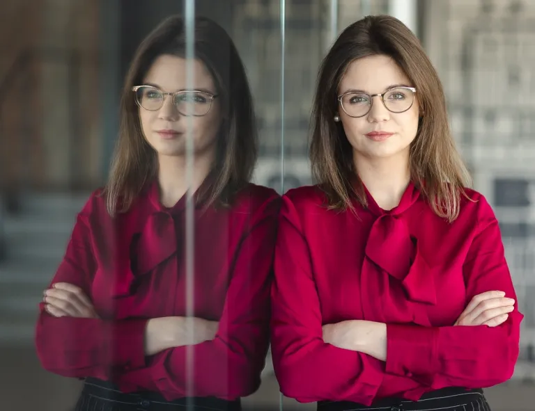 HR menedżer | Studia podyplomowe w Opolu | Uniwersytet WSB Merito Opole: Uczestniczka studiów podyplomowych opiera się z założonymi rękami o szklaną szybę.