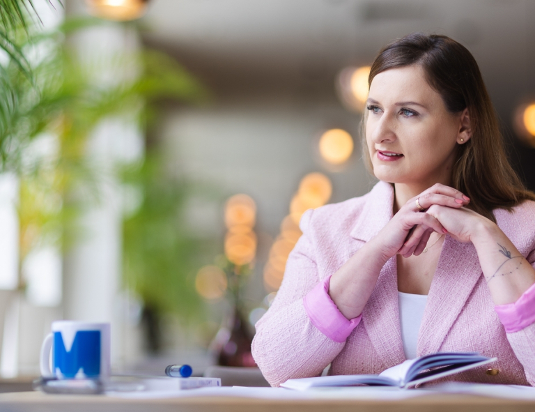 Psychodietetyka  dzieci i młodzieży | Studia podyplomowe w Opolu | Uniwersytet WSB Merito Opole: Uczestniczka studiów podyplomowych siedząca przy biurku z otwartym notatnikiem, spogląda za okno.