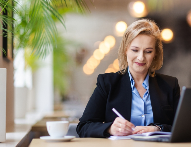 Zamówienia publiczne | Studia podyplomowe w Opolu | Uniwersytet WSB Merito Opole: Uczestniczka studiów podyplomowych siedząca przy biurku z laptopem i robiąca notatki