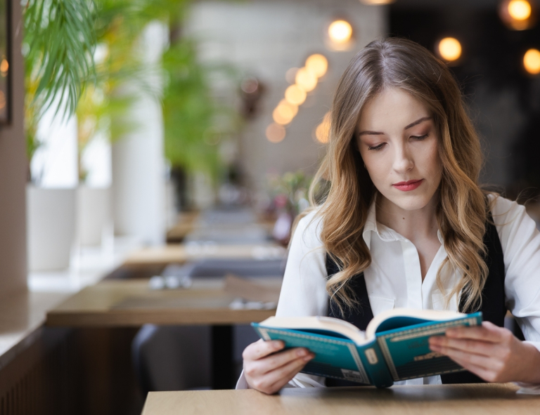 Warsztat pracy pedagoga-wychowawcy | Studia podyplomowe w Opolu | Uniwersytet WSB Merito Opole: Uczestniczka studiów podyplomowych siedzi przy stoliku i czyta książkę