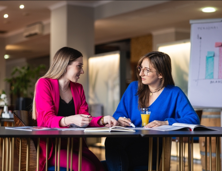 Księgowość i podatki w praktyce, studia podyplomowe: Uczestniczki studiów podyplomowych siedzą przy biurku i rozmawiają 