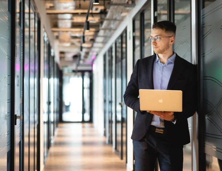 Coaching w standardzie ICF | Studia podyplomowe w Opolu | Uniwersytet WSB Merito Opole: Uczestnik studiów podyplomowych opiera się o ścianę z laptopem w reku