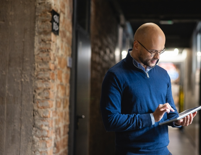 Interwencja kryzysowa | Studia podyplomowe w Opolu | Uniwersytet WSB Merito Opole: Uczestnik studiów podyplomowych stoi w korytarzu z tabletem w ręce