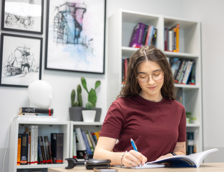 Dietetyka | Studia II stopnia ze studiami podyplomowymi w Opolu | Uniwersytet WSB Merito Opole: Uczestniczka studiów podyplomowych siedzi przy stoliku i czyta książkę