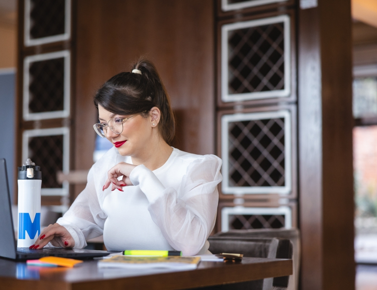 Zarządzanie logistyką w służbach mundurowych | Studia podyplomowe w Opolu | Uniwersytet WSB Merito Opole: Uczestniczka studiów podyplomowych siedzi przy biurku i pracuje przy laptopie