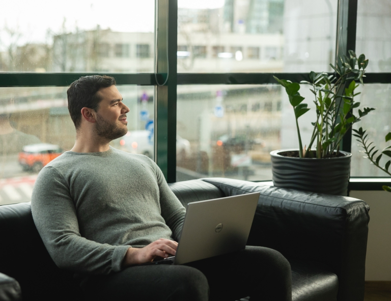 Inżynieria oprogramowania w JavaScript (TypeScript) | Studia podyplomowe w Opolu | Uniwersytet WSB Merito Opole: Uczestnik studiów podyplomowych siedzi na kanapie i pracuje na laptopie