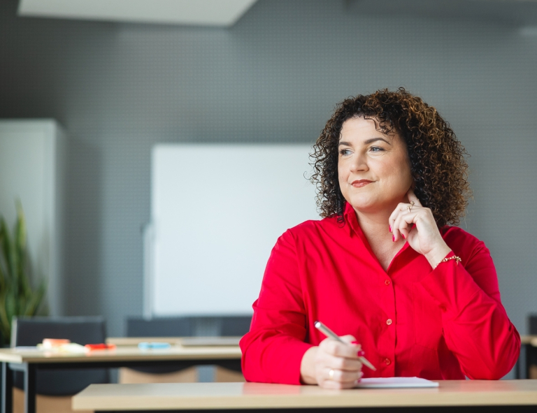 Innowacje w zarządzaniu jednostkami administracji | Studia podyplomowe w Opolu | Uniwersytet WSB Merito Opole: Uczestniczka studiów podyplomowych robi notatki przy biurku i spogląda przez okno