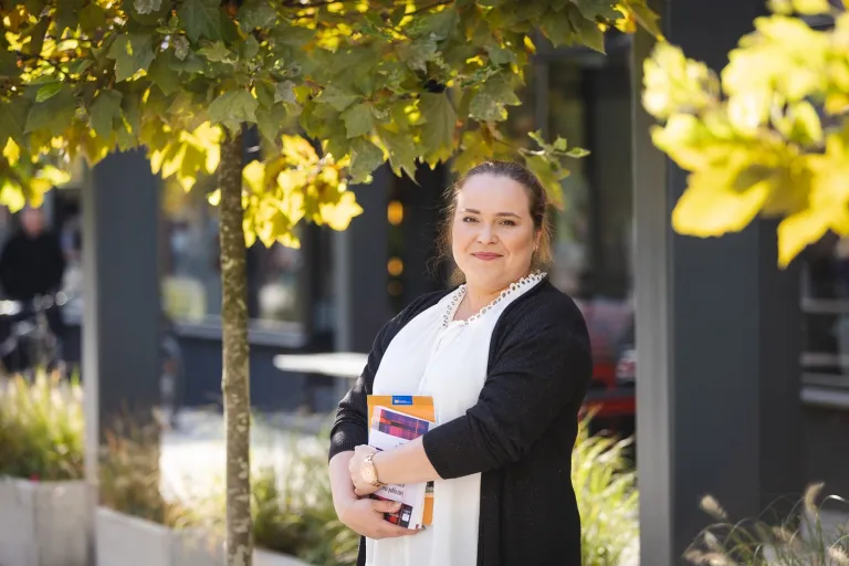 International Management | Uniwersytet WSB Merito Opole: Kobieta stojąca na zewnątrz kawiarni, w rękach trzyma książki