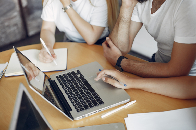 Komunikacja w organizacji | Szkolenia i kursy w Poznaniu | Uniwersytet WSB Merito w Poznaniu: Grupa osób pracuje wspólnie przy laptopie, zapisując notatki