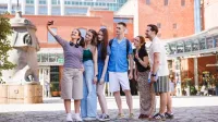 Administracja gospodarcza | Uniwersytet WSB Merito w Poznaniu: Grupa uśmiechniętych studentów wykonuje sobie selfie przed budynkiem starego browaru. 