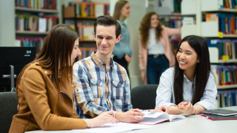 Zarządzanie gospodarką komunalną | Studia II stopnia ze studiami podyplomowymi  | Uniwersytet WSB Merito w Poznaniu: Troje studentów uczy się wspólnie przy stole w bibliotece, śmiejąc się