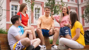 Innowacyjne Zarządzanie Publiczne | Studia II stopnia w Poznaniu | Uniwersytet WSB Merito w Poznaniu: 5 studentów siedzi na ławce w centrum miasta i rozmawiają w wesołej atmosferze