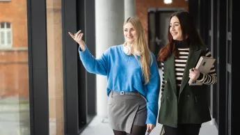 Green Leader | Uniwersytet WSB Merito w Poznaniu: Dwie studentki, kolorowo ubrane spacerują po korytarzu uczelni WSB Merito w Poznaniu 
