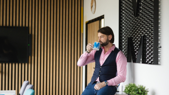 Trener języków obcych | Studia podyplomowe w Poznaniu | Uniwersytet WSB Merito w Poznaniu: Mężczyzna pijący z kubka Merito w zrelaksowanej pozie