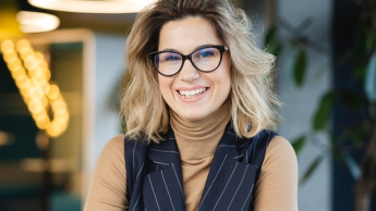 Zarządzanie zespołami rozproszonymi | Studia podyplomowe w Poznaniu | Uniwersytet WSB Merito w Poznaniu: Uśmiechnięta kobieta w okularach przy biurku