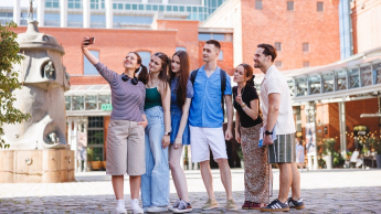 Administracja gospodarcza | Uniwersytet WSB Merito w Poznaniu: Grupa uśmiechniętych studentów wykonuje sobie selfie przed budynkiem starego browaru. 