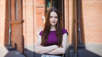 Psychologia Komunikacji | Studia jednolite magisterskie w Poznaniu | Uniwersytet WSB Merito w Poznaniu: Studentka pozująca do zdjęcia przed nowoczesnym budynkiem uczelni.