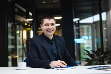 Zasady rekrutacji | Uniwersytet WSB Merito w Poznaniu: Uczestnik studiów MBA siedzi na korytarzu przy stole uczelni- Uniwersytet WSB Merito w poznaniu