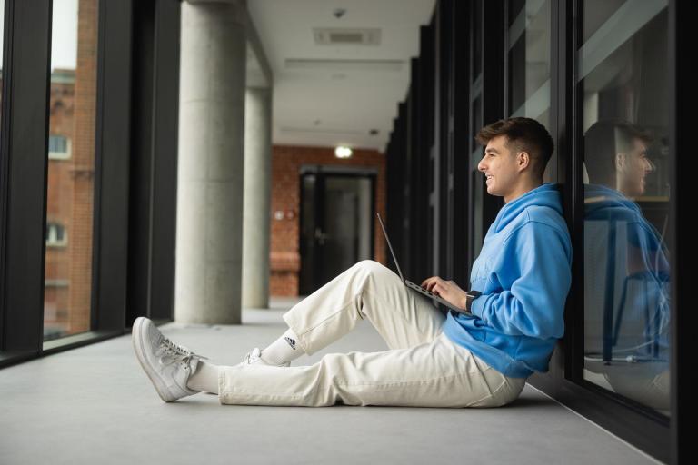 Cyfrowy uniwersytet | Uniwersytet WSB Merito w Poznaniu: Poznań - student w korytarzu z laptopem