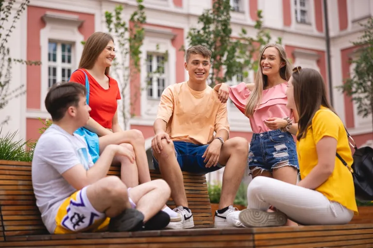 Archiwum X WSB Merito na tropie jamy chwilowej | Uniwersytet WSB Merito w Poznaniu: 5 studentów siedzi na ławce w centrum miasta i rozmawiają w wesołej atmosferze