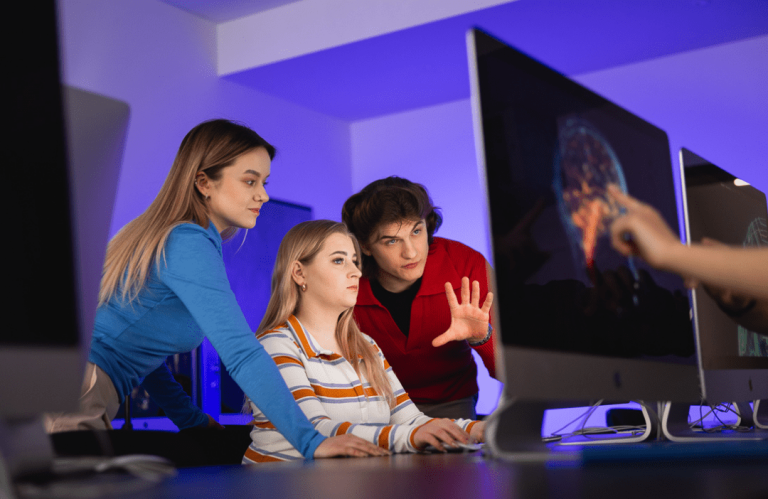 Claude CLI - warsztat techniczny (hands-on) | Szkolenia i kursy w Poznaniu | Uniwersytet WSB Merito w Poznaniu: grupa studentów omawia projekt przed monitorem