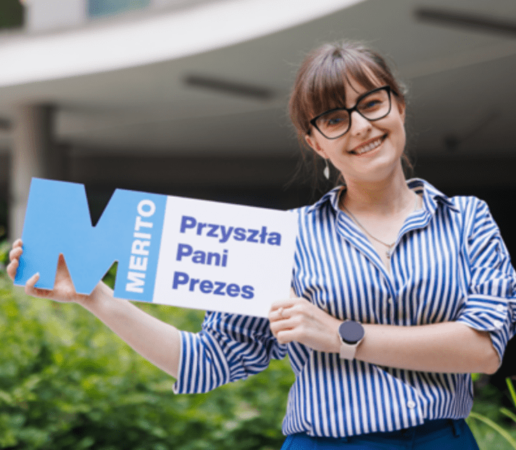"Potrafię się obronić" – sprawdź, jak ogarnąć stres przed obroną! 🎓 | Aktualności | Uniwersytet WSB Merito w Poznaniu: brunetka w okularach trzyma plakietke "przyszła pani presez"