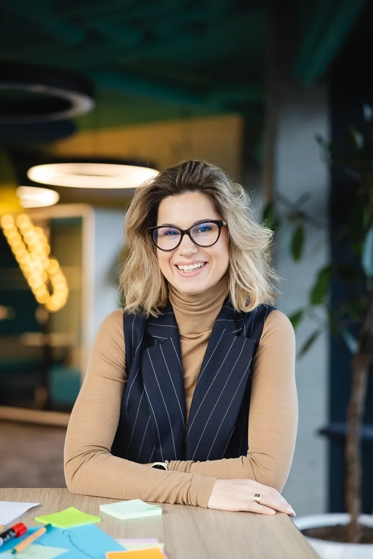 Weź udział w sesji zdjęciowej i zostań twarzą Uniwersytetu WSB Merito! | Aktualności | Uniwersytet WSB Merito w Poznaniu: Uśmiechnięta kobieta w okularach przy biurku