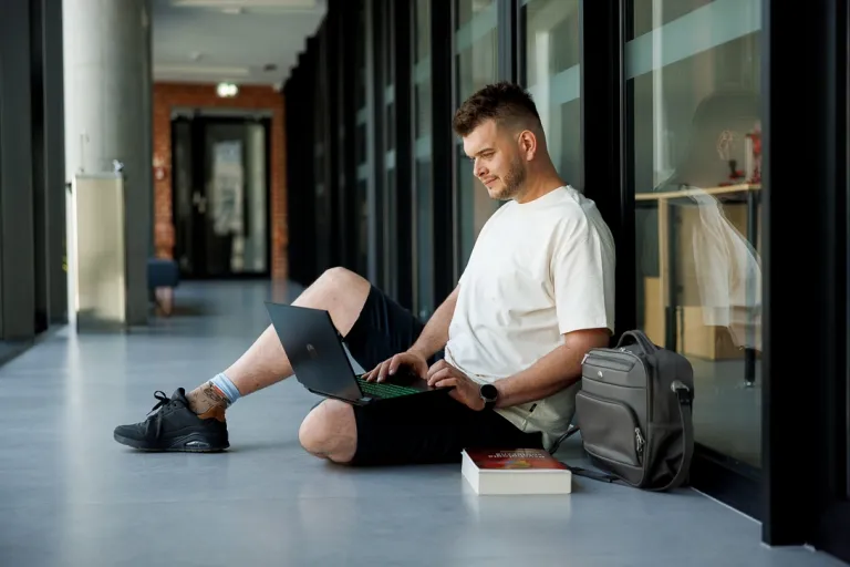 Marketing i sprzedaż | Studia I stopnia w Poznaniu | Uniwersytet WSB Merito w Poznaniu: chłopak pracuje na laptopie siedząc na podłodze na korytarzu