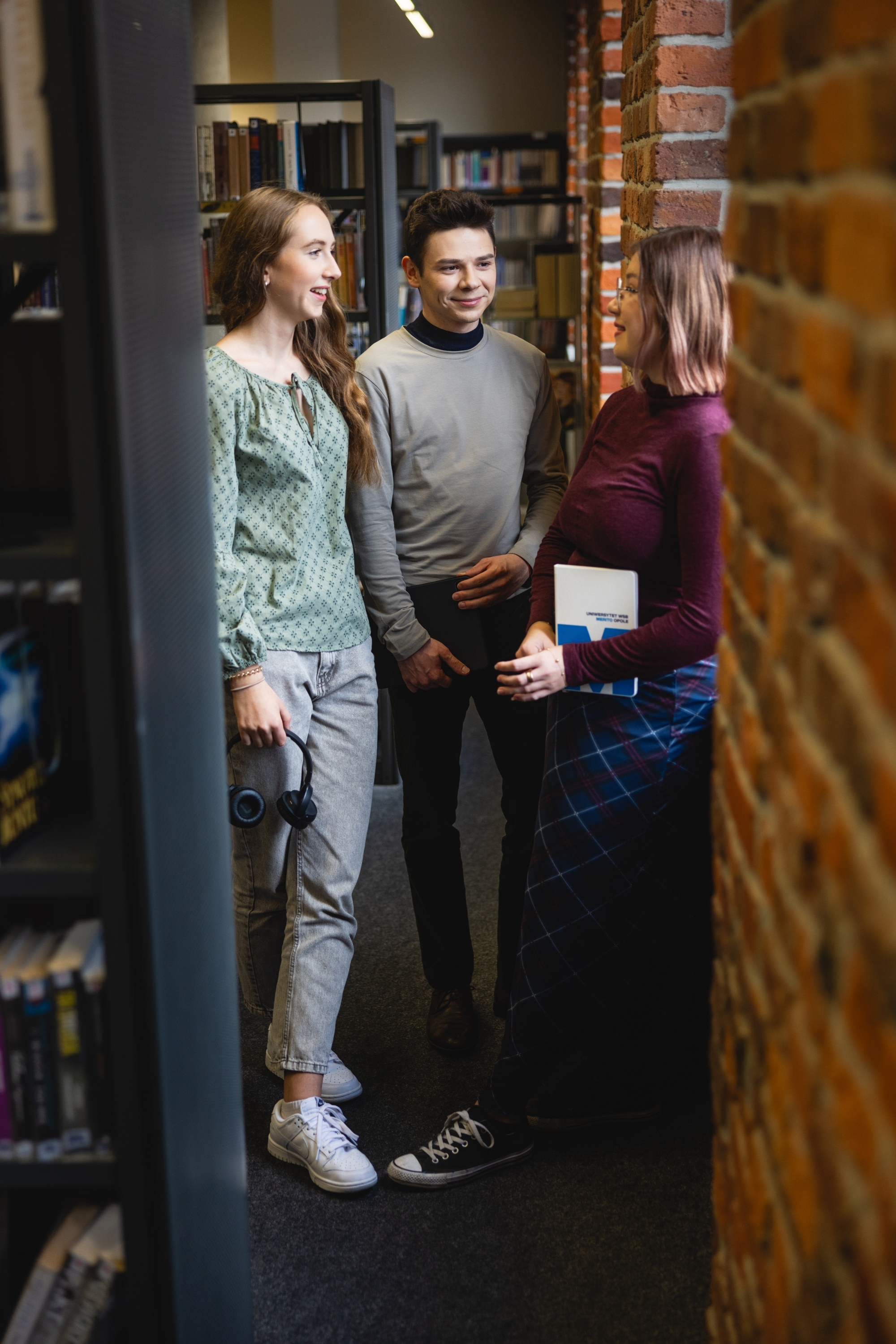 Troje młodych ludzi stojących między półkami w bibliotece