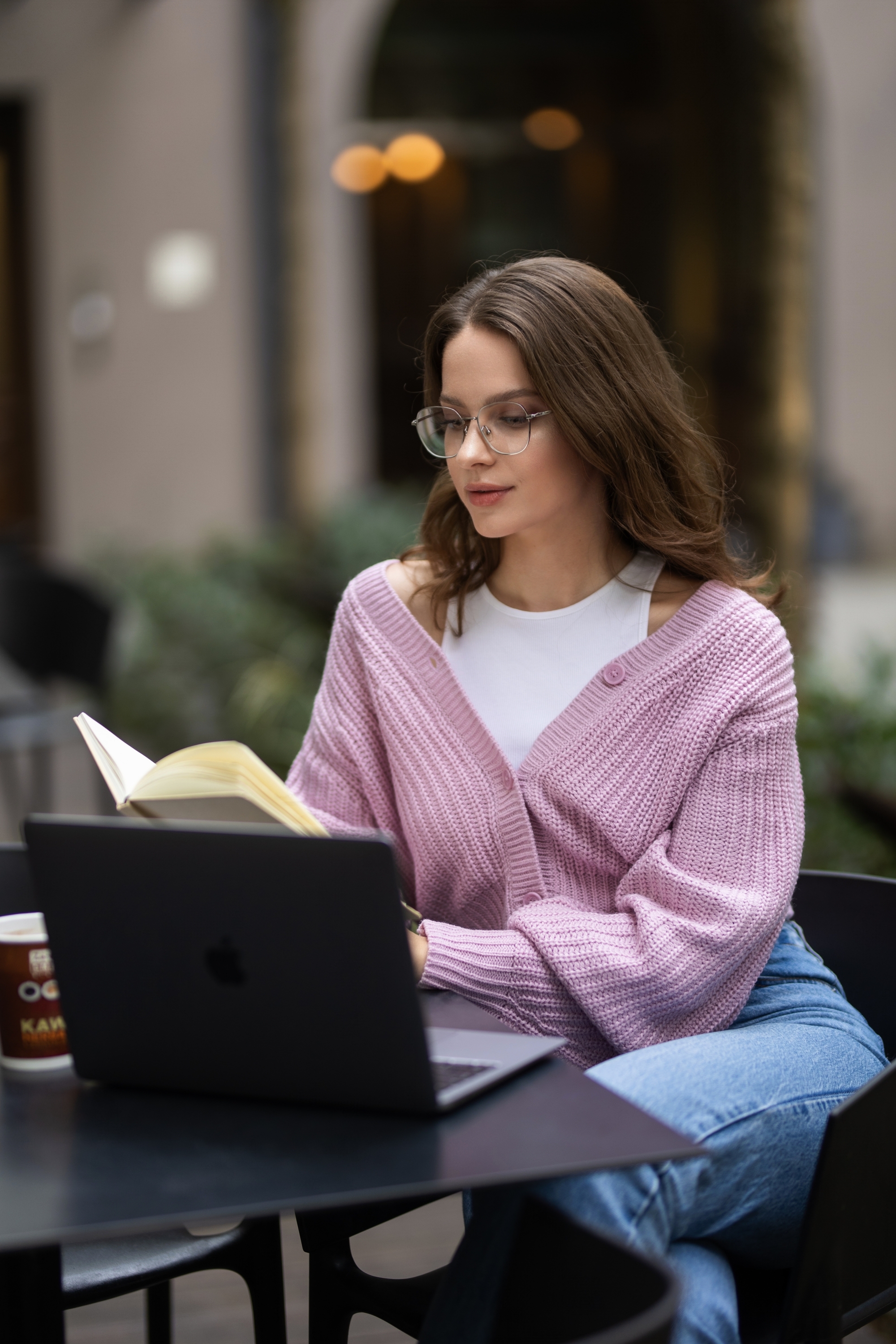 Dziewczyna czytająca książkę przy biurku, obok leży laptop