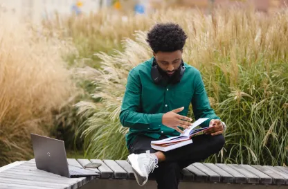Blog "Okiem Praktyków" | Uniwersytet WSB Merito: Mężczyzna siedzący na dworze przy laptopie i książkach