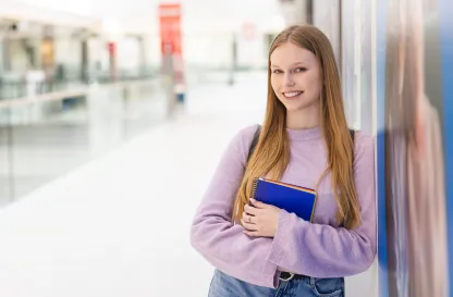 Poradniki - dzielimy się wiedzą | Uniwersytet WSB Merito: Dziewczyna oparta o ścianę z notatnikiem w dłoni