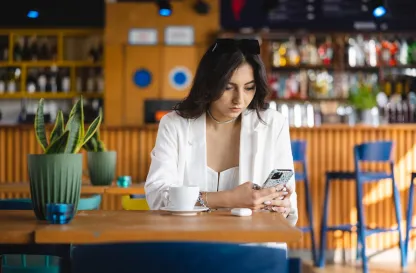 Poradniki - dzielimy się wiedzą | Uniwersytet WSB Merito: Grafika główna: Uniwersytety WSB Merito, praca, cv, dziewczyna siedzi przy stole i przegląda telefon