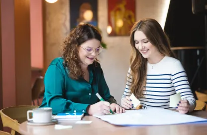 Blog "Okiem Praktyków" | Uniwersytet WSB Merito: Dwie kobiety rozmawiające i pracujące przy stole