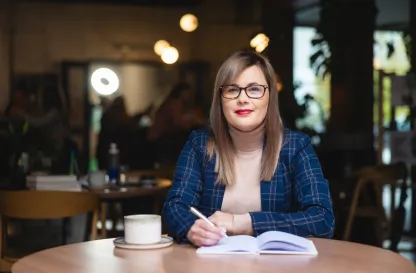 Blog "Okiem Praktyków" | Uniwersytet WSB Merito: Kobieta elegancko ubrana siedząca przy stole.